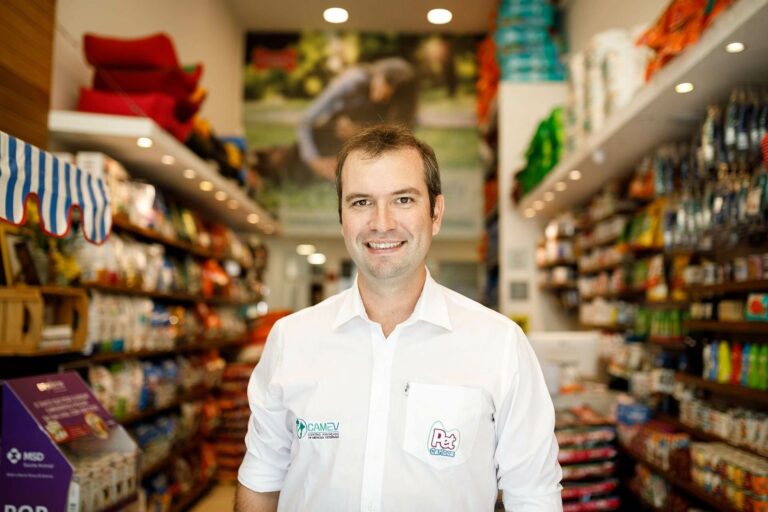 Homem branco, dono de petshop, sorri em corredor de petshop